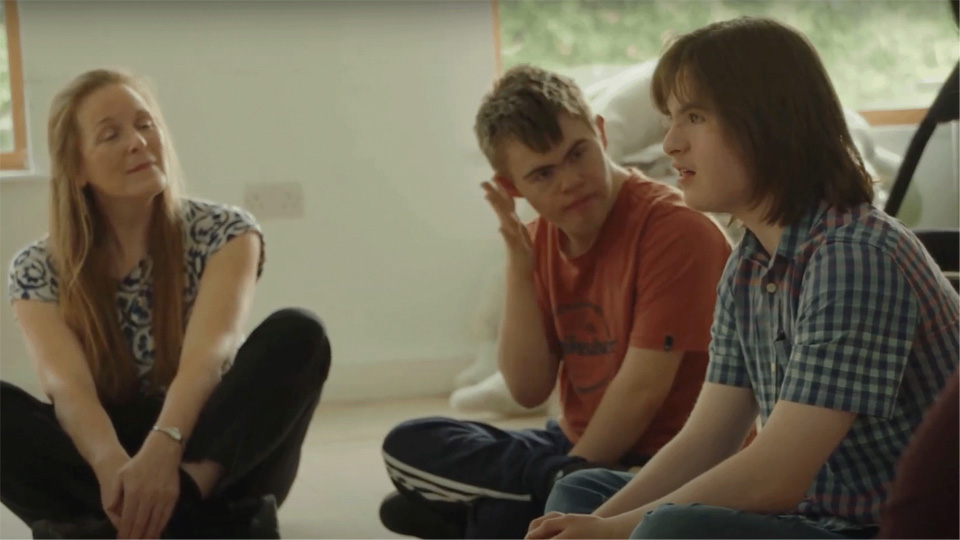 A man sitting in a circle with other young adults talking, with a women sitting next to them listening.